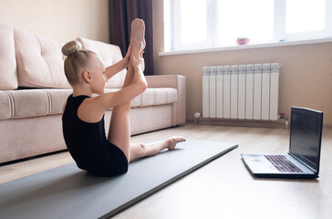 The child watches online video on a laptop and performs sports exercises - yoga, gymnastics. Stay at home. Self-isolation, quarantine, online education concept.