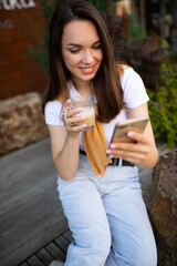charming free young woman in casual look is drinking coffee while sitting in a summer park
