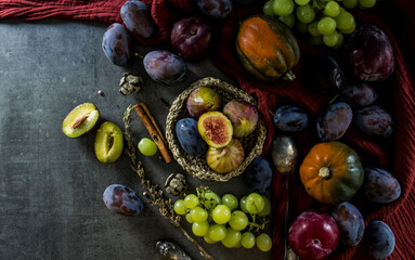 Fresh fruits and vegetables on a table. Top view photo of grapes, pumpkins, plums and figs. Grey textured background. Autumn still life.