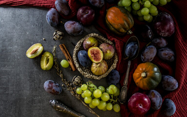 Fresh fruits and vegetables on a table. Top view photo of grapes, pumpkins, plums and figs. Grey textured background. Autumn still life.