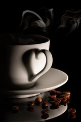 Cup of hot coffee with smoke and coffee beans on black background. A shadow in the shape of a heart.