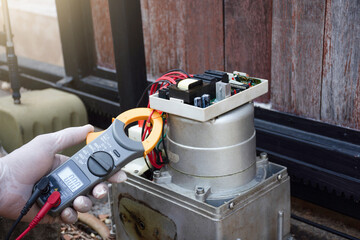 Technician man hand pressing remote control while repair and using digital clamp meter to test and...