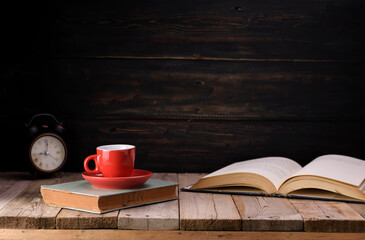 Red coffee cup with dark black coffee placed on the old green book And the clock is arranged on an...