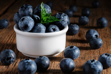 Ripe blueberries in drops of water with a leaf of fragrant mint on a wooden background.