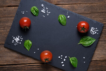 Template. Cherry tomatoes, Basil leaves, chilli pepper and large sea salt on a slate. The view from the top.