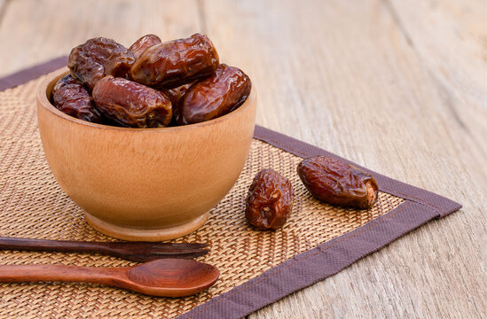 Closeup date palm fruits in wooden bowl isolated on wood table background. 