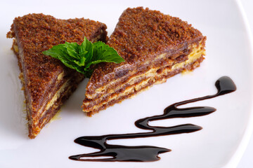 Two pieces of honey cake on a white plate with a mint lea