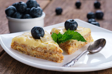 Almond cake with blueberries and mint in a white plate on a wooden table.