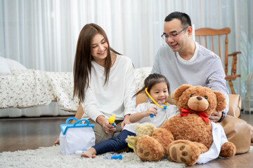 Happy young father and mother and a little daughter playing with Toy, sitting on the floor in living room, family, parenthood and people concept