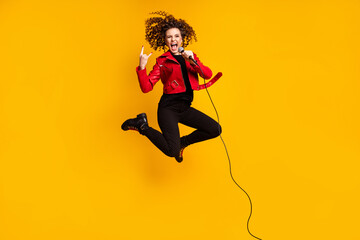Full length body size view of nice cheerful ecstatic cool crazy wavy-haired girl jumping singing showing horn sign isolated on yellow color background