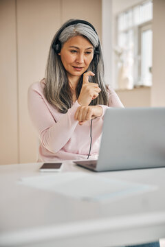 Concentrated adult female in headphone working online with another people from home office