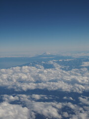 Bird's eye view of snowy Mount Fuji with white clouds over blue sky in Japan in winter