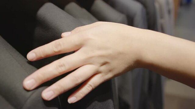 close up asian female customer hand toch choose suit rack in tailor suit store.female person make purchase suit jacket