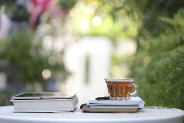 Transparent tea cup and tablet with books on white metal table at outdoor
