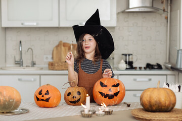 Happy halloween. Cute little girl in witch costume with carving pumpkin. Happy family preparing for Halloween. girl lights candles