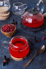 Hot cranberry tea in a glass Cup and a teapot on a dark cold background. Warming and healing tea with berries. New year's drink for a cozy evening.