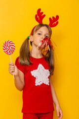 Little girl holding big lollipop and blowing party whistle