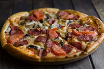 pizza with sausages, tomatoes and herbs, on a wooden background