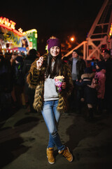The beautiful young lady standing at the Christmas fair near carousel and eating pop corn 