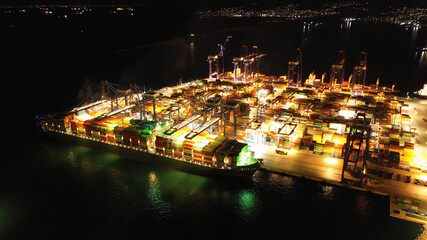 Fototapeta premium Aerial drone night shot of illuminated container terminal facilities in popular Mediterranean logistics port