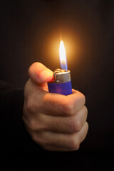 Person lighting a blue lighter with his hand on a dark, unfocused background