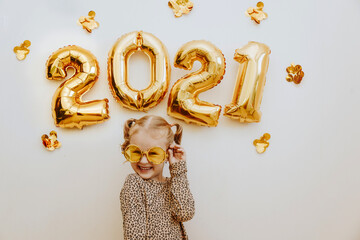 Little girl wearing gold masquerade glasses smiling and fooling around, celebrating Christmas and New Year at home.