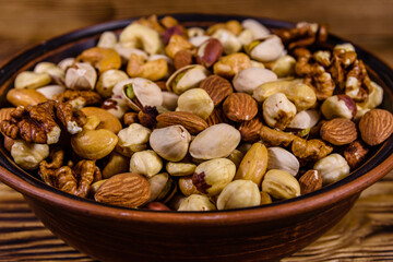 Various nuts (almond, cashew, hazelnut, pistachio, walnut) in ceramic plate on a wooden table. Vegetarian meal. Healthy eating concept