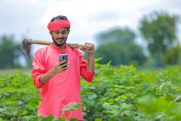 Young indian farmer using smartphone in cotton field