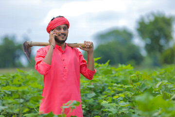 Young indian farmer talking smartphone in cotton field