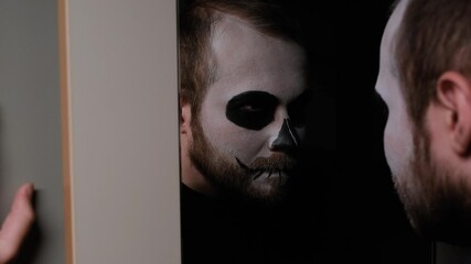 A man in zombie make-up in bathroom in front of the mirror and looks at himself.