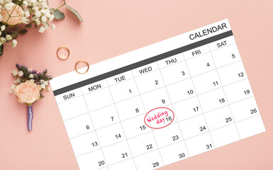 Wedding day marked on calendar, gold rings and bouquet over pink background