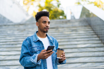 Portrait of smiling african american man looking at cellphone holding coffee on the street
