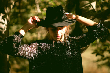 Trendy girl in the woods wearing a black dress and a fedora hat during autumn in Spain.