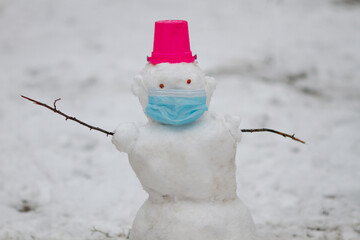 Snowman wearing protection mask standing outdoors on playground on a snowy winter day. Covis...