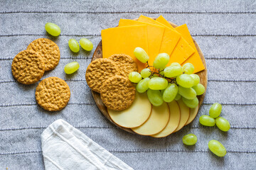 Cheese, green grapes and biscuits on the wooden tray on the gray table cloth
