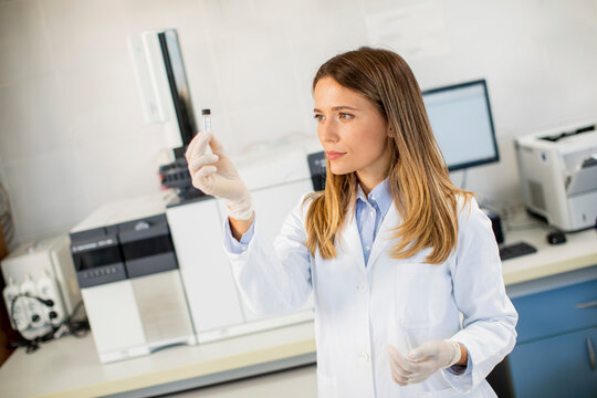 Female scientist in a white lab coat preparing vial with a sample for an analysis on a gas chromatograph in biomedical lab