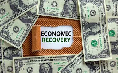 The text 'economic recovery' appearing behind torn brown paper. Dollar bills. Business concept.