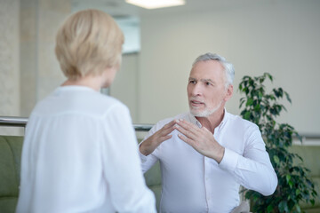 Bearded gray-haired man and blonde woman talking using sign language