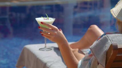 Anonymous stylish woman relaxing on sunbed at poolside with cocktail