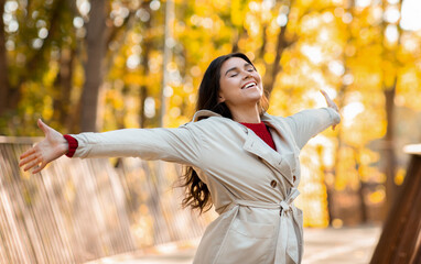 Cheerful young lady in fashionable autumn clothes feeling free and happy at autumn park, panorama