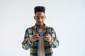 Portrait of a cheerful young african man dressed in plaid shirt playing games on mobile phone isolated over white background