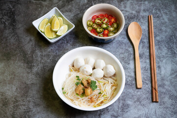 Rice stick noodles with fish ball and garlic cracklings with lard in white bowl; pickled chili condiment on table.