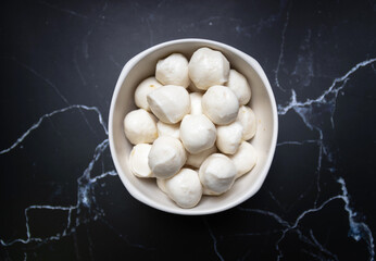Boiled fish balls in white bowl on black marble table with copy space; top view