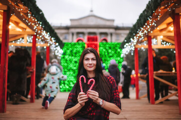 The beautiful young lady standing near Christmas house and keeping two christmas candies 