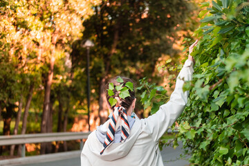 Woman with green leaves in hair on green park backdrop. Greening concept. Save planet. Environmental awareness. Growing plant's.