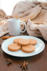 Living room details in winter. Close-up of a white mug with an infusion on a wooden table with anise and cinnamon, a cream colored blanket and cookies. Homey winter concept.
