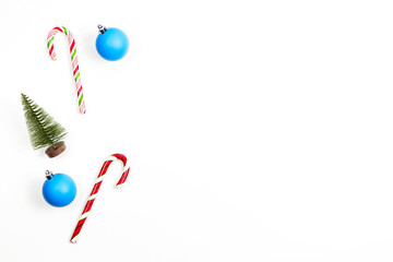 Minimal Christmas background. Candy canes, little Xmas tree and blue Xmas decoration bauble balls on white background. Top view