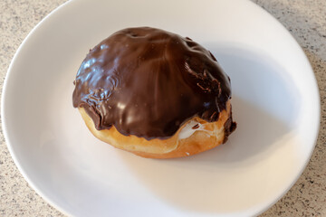 A chocolate cover cream filled donut on a white plate atop a kitchen counter.