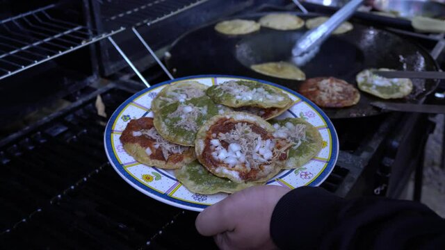 Plate being filled with freshly made traditional mexican dish chalupas with red and green salsa, onion and pork meat