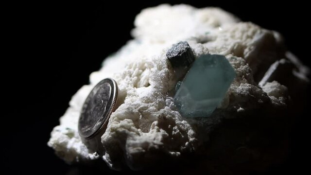 A single aquamarine crystal in a matrix of feldspar with a dime as a size reference.
